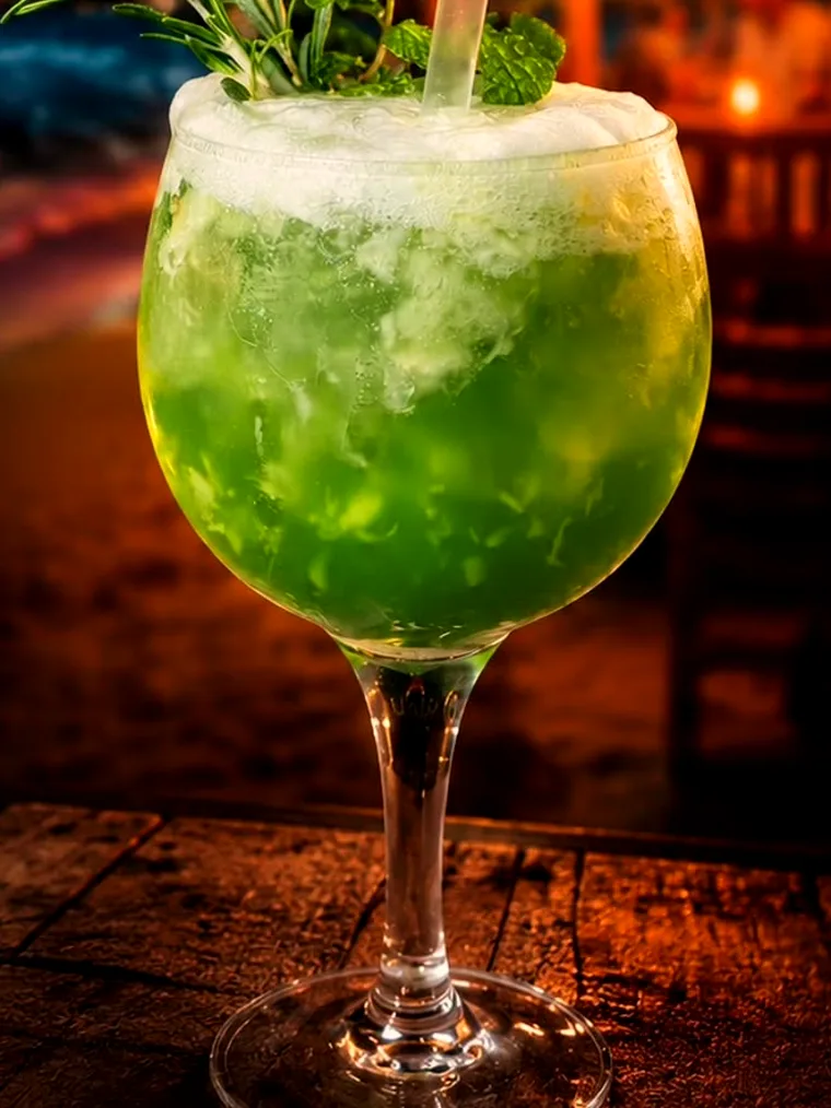Drink Sunset Chalé: taça com drink verde, gelo e ramos de alecrim