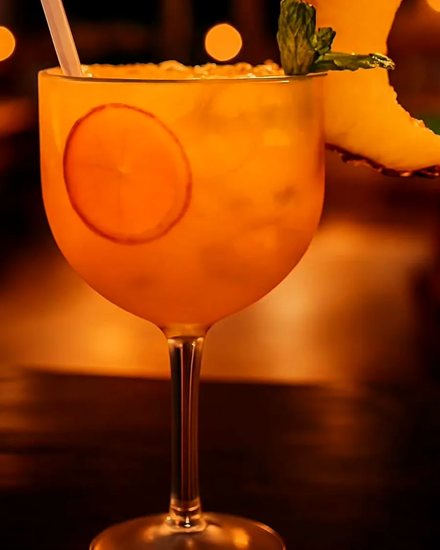 Drink cítrico com fatia de abacaxi e luzes quentes ao fundo