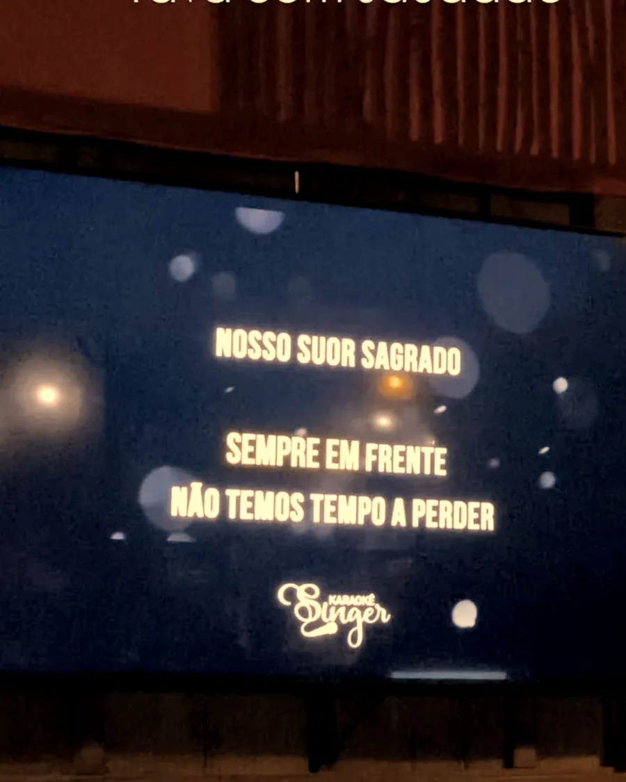 Telão de karaokê com a letra da música aparecendo no salão do Chalé
