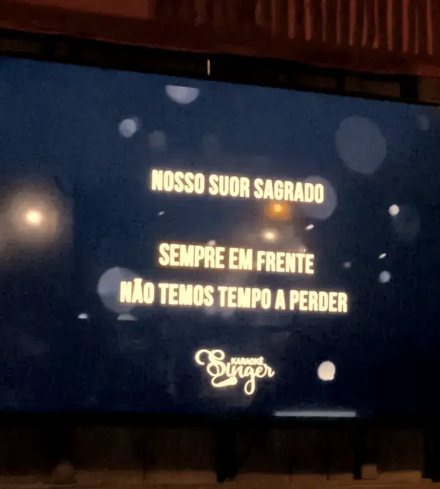 Telão de karaokê com a letra da música aparecendo no salão do Chalé