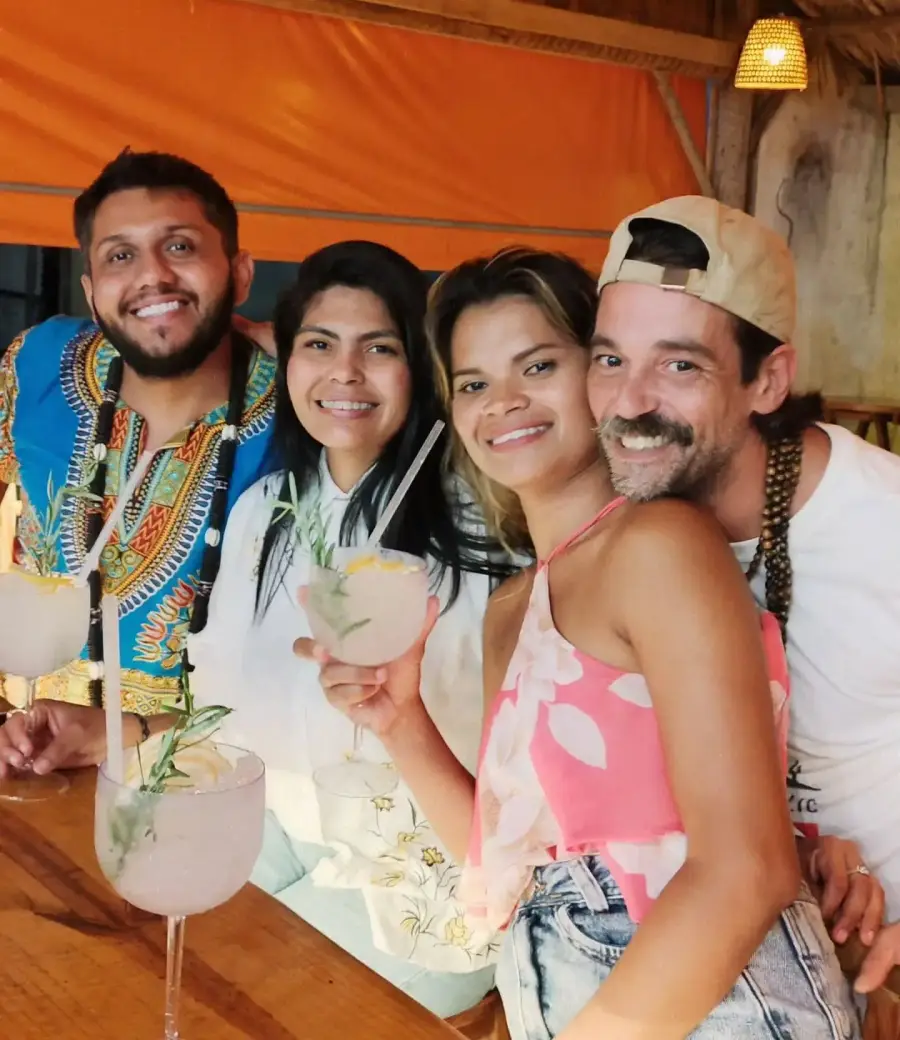 Quatro amigos brindando com drinks embaixo do toldo laranja do Chalé, de dia