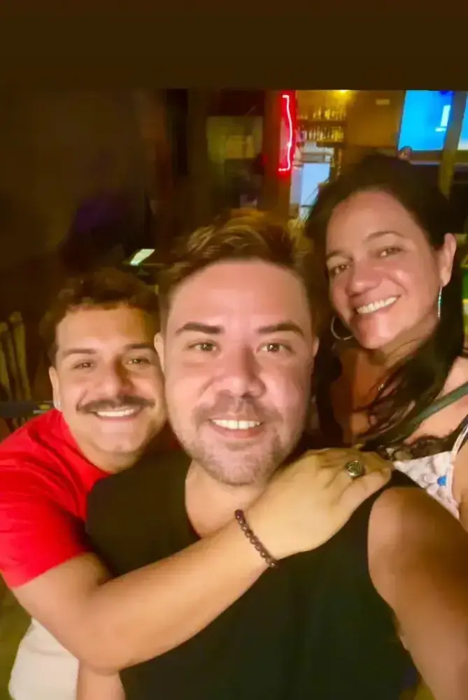 Três amigos numa selfie com o balcão e o letreiro de neon atrás