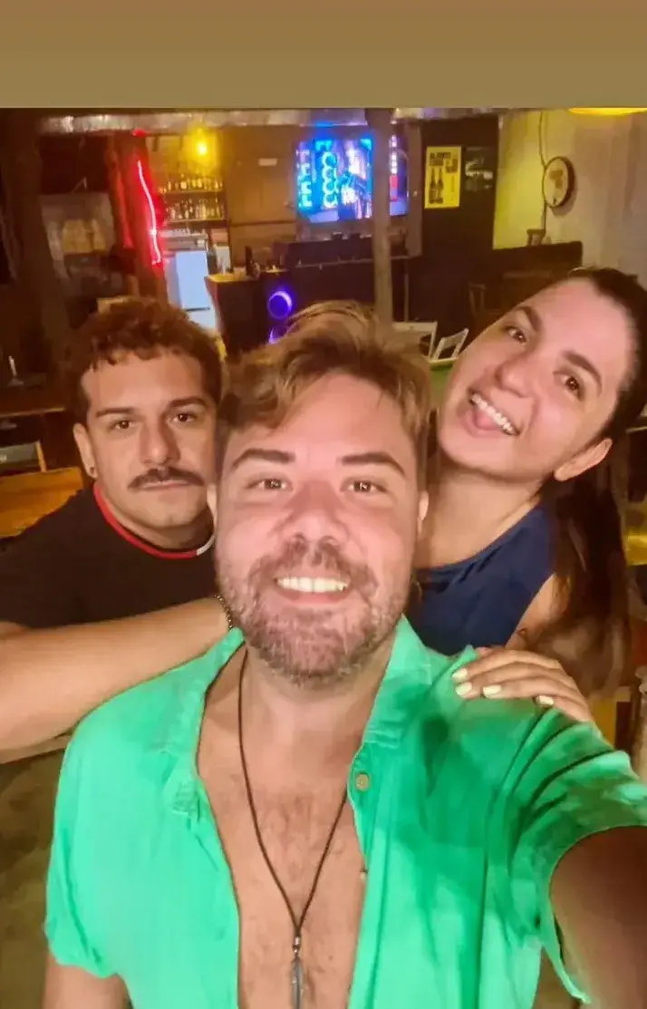 Selfie de três clientes com o bar iluminado ao fundo