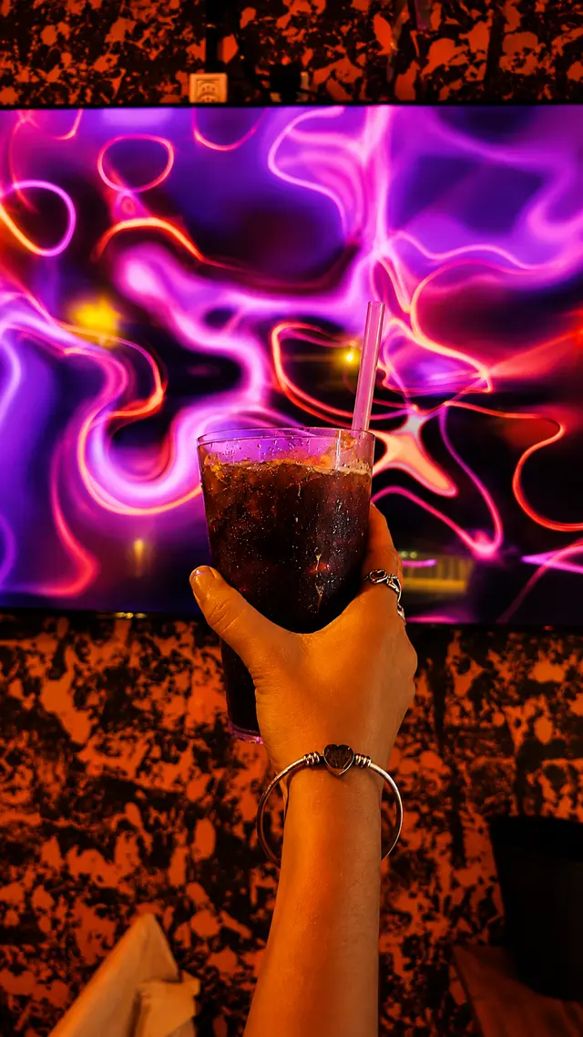 Copo com drink na mão em frente ao telão com luzes de neon do Chalé