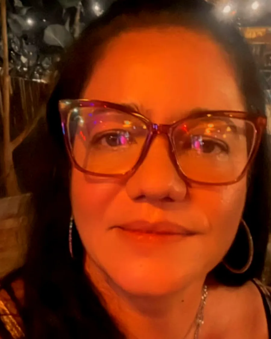 Cliente sorrindo sob a luz quente do salão, com as lâmpadas do Preá ao fundo