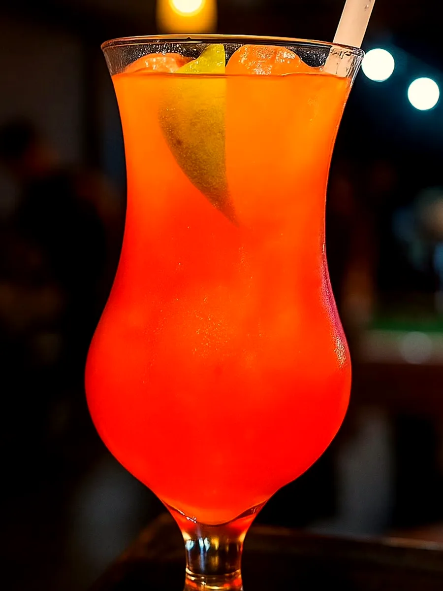 Taça alta com drink alaranjado e uma fatia de laranja