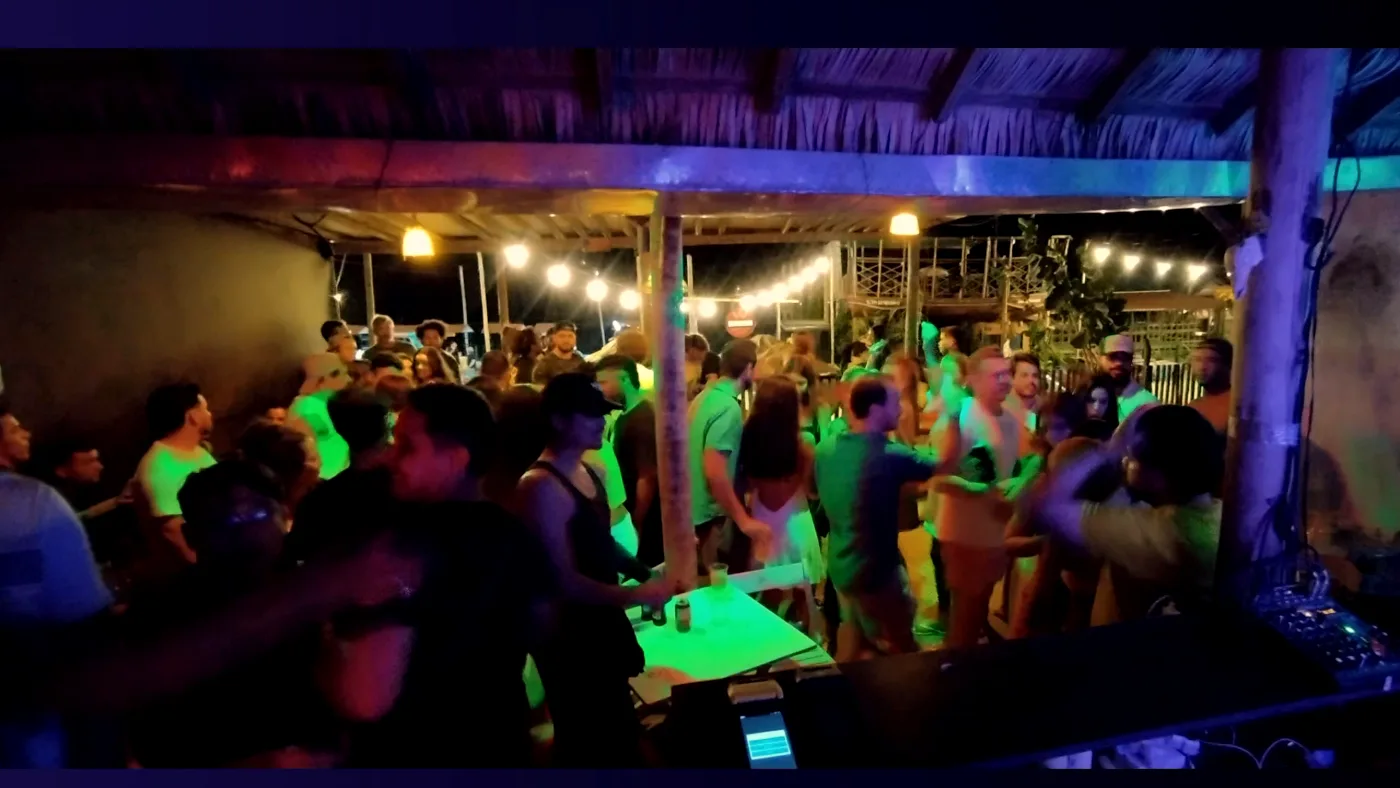 Salão lotado à noite, luzes coloridas e pessoas em pé entre as mesas