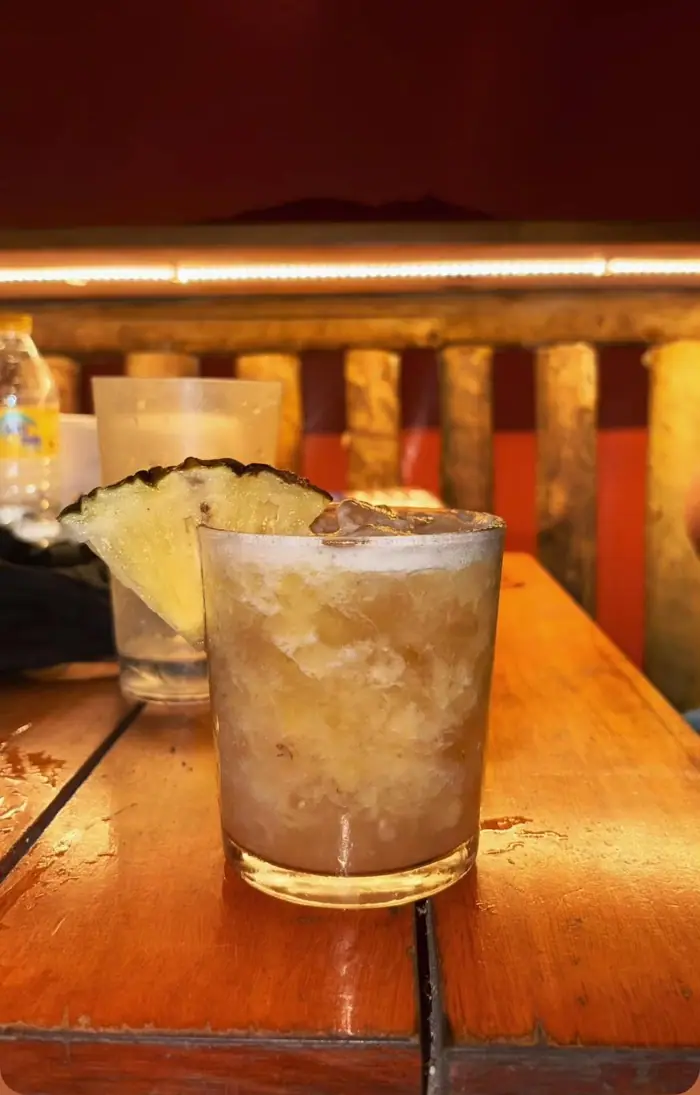 Copo baixo com drink de abacaxi e gelo picado sobre a mesa de madeira do Chalé